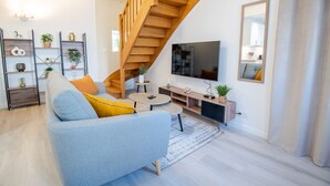 Een moderne woonkamer met een trap, een bank, een salontafel, een televisie en een boekenkast.
