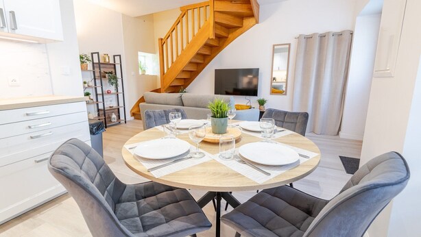 Een moderne eetruimte met een ronde tafel voor vier personen, een trap en een zithoek met een bank en televisie.