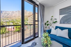 Ein Balkon mit Blick auf eine gebirgige Landschaft, ein blaues Sofa mit gemusterten Kissen und ein Blumentopf.
