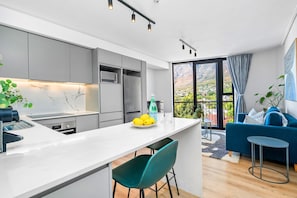 Eine moderne Küche mit Marmorfliesenspiegel, ein Essbereich mit weißem Tisch und ein blaues Sofa in einem Wohnraum mit Blick.