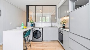 Une cuisine moderne équipée d’un lave-linge intégré, de tabourets de bar et d’une grande fenêtre.