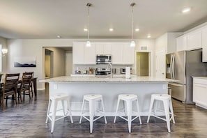 Una cocina moderna con una isla central, taburetes blancos y electrodomésticos de acero inoxidable.