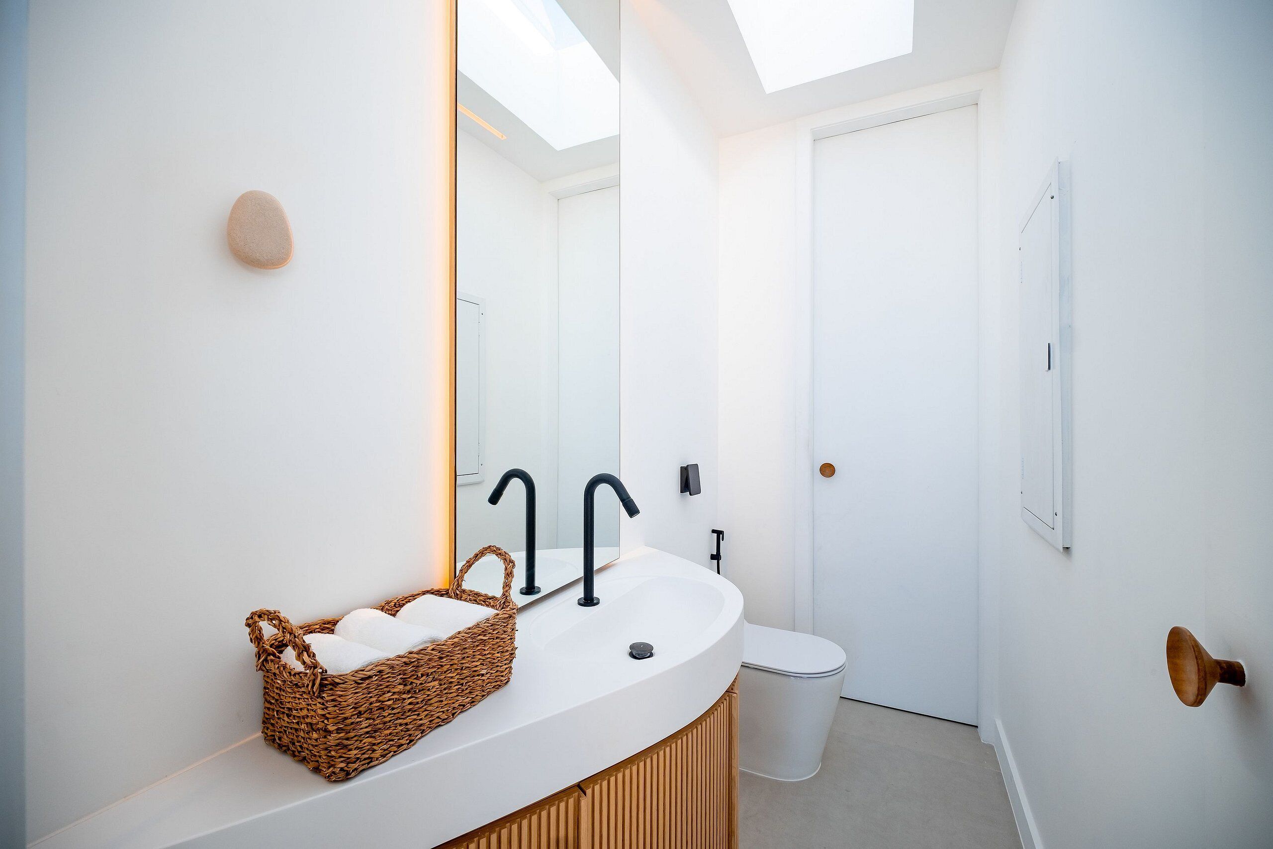 Ein modernes Badezimmer mit einem weißen Waschbecken, einem schwarzen Wasserhahn und einem Korbwäscheschrank.