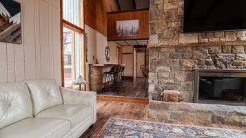 A living room with a stone fireplace, a leather sofa, and a television mounted on the wall.