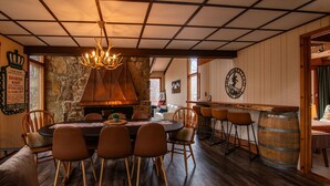 Uma sala de jantar com uma mesa redonda, cadeiras, um candelabro, uma parede de pedra e um barril de madeira.