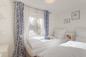 A bedroom with two beds, a bedside table with books, and a window with curtains. - Holiday Home on the Backwaters, Lutow (Luetow)