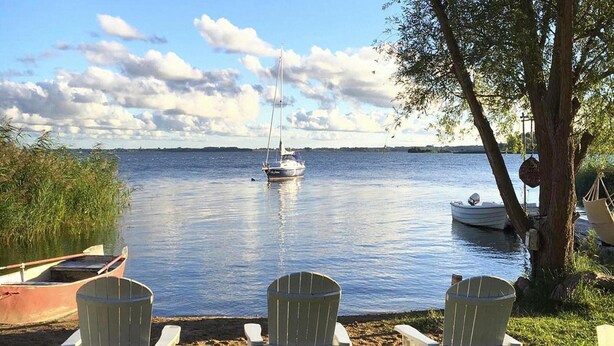 Three Adirondack chairs facing a calm lake with boats and a tree on the shore. - Holiday Home on the Backwaters, Lutow (Luetow)