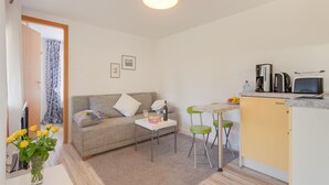 Un espacio habitable compacto con sofá, una mesita, kitchenette y comedor con sillas.