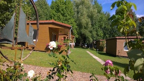 Una cabaña de madera con porche, rodeada de un césped cuidado y plantas en flor.