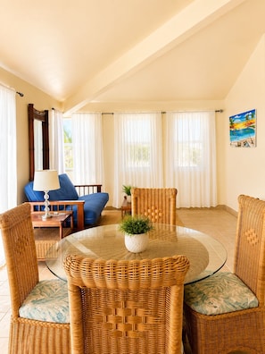 A room with a round glass table, wicker chairs, a blue sofa, a lamp, and a painting of a beach scene. - Tranquil North Ambergris Caye Retreat - 3BR Home - Sleeps 8 (San Pedro)