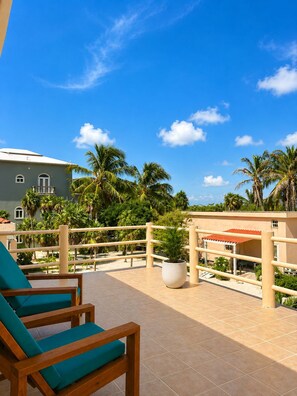 A terrace with a wooden chair, a potted plant, and a view of palm trees and a building. - Tranquil North Ambergris Caye Retreat - 3BR Home - Sleeps 8 (San Pedro)