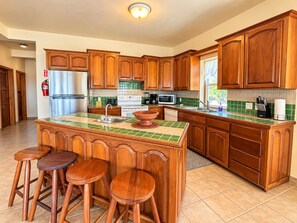 Eine Küche mit Holzausstattung, einem Edelstahlkühlschrank, einer Mikrowelle und einer großen Kochinsel mit Hockern.