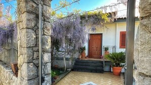A stone pillar, a tiled patio, a wooden door, and a garden with purple flowers. - Cozy facility, located in a quiet place a few minutes from the sea (Vico Equense)