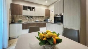 A modern kitchen with built-in appliances, a dining table with a fruit bowl, and a view of the living area. - Cozy facility, located in a quiet place a few minutes from the sea (Vico Equense)