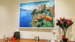 A painting of a coastal scene with buildings, cacti, and a vase of tulips on a wooden table. - Cozy facility, located in a quiet place a few minutes from the sea (Vico Equense)