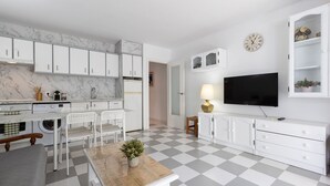 Eine moderne Küche mit weißen Schränken, einer Marmor-Spritzschutzleiste, einem Essbereich mit Tisch und Stühlen, einem Fernseher und einem Schachbrettboden.