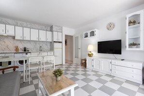 A modern kitchen with white cabinets, a marble backsplash, a dining area with a table and chairs, a TV, and a checkered floor. - Apartment with pool near Cala Capellans (Salou)