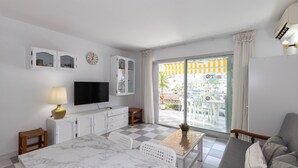 Ein Hotelzimmer mit Schachbrettboden, einem Fernseher, einer Couch, einem Esstisch und einem Balkon mit Blick.