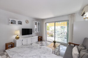 A hotel room with a checkered floor, a television, a sofa, a dining table, and a balcony with a view. - Apartment with pool near Cala Capellans (Salou)