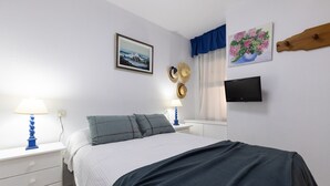 Ein Schlafzimmer mit einem Bett, zwei Nachttischen mit Lampen, einem Fernseher und Wanddekorationen, darunter ein gerahmtes Bild und ein Gemälde.