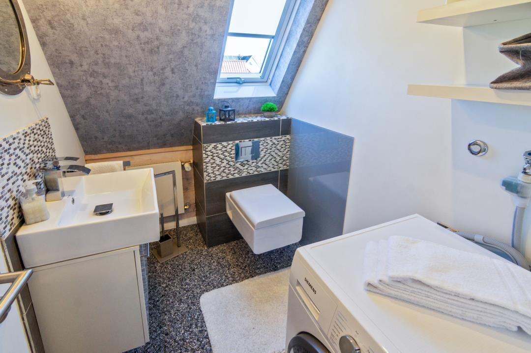 Casa de banho compacta com clarabóia, uma pia, sanita, máquina de lavar roupa e um porta-toalhas.