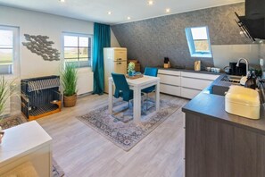 A modern kitchen with a dining area, a built-in refrigerator, and a window providing natural light. - The exclusive Tide vacation apartment in Hilgenriedersiel boasts high-quality comfort, a box-spring bed and a terrace. Ideal for 2 people, quietly located near the North Sea and the Wadden Sea - perfect for relaxing days in East Frisia. (Hagermarsch)