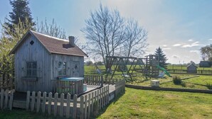 A wooden cabin with a fenced deck, a playground with a slide, and a grassy field. - Vacation apartment Treibholz | Quiet North Sea vacation Hilgenriedersiel (Hagermarsch)