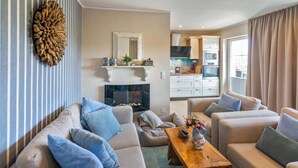 A living room with a fireplace, sofas, a coffee table, and a kitchen in the background. - Vacation apartment Treibholz | Quiet North Sea vacation Hilgenriedersiel (Hagermarsch)