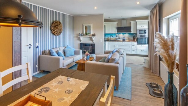 A modern living room with a dining table, sofas, a fireplace, and a kitchen in the background. - Vacation apartment Treibholz | Quiet North Sea vacation Hilgenriedersiel (Hagermarsch)