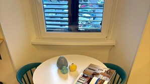 Ett runt bord med ett tidningsställ, två vaser och ett fönster med persienner.