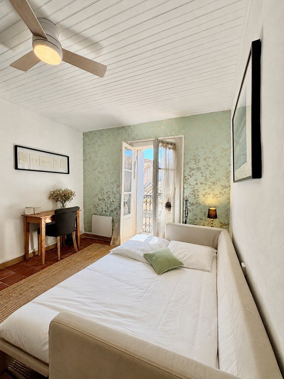 A bedroom with a bed, a desk, a chair, a radiator, and a ceiling fan.