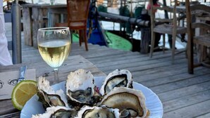 Une terrasse en bois avec une assiette d’huîtres et un verre de vin blanc.