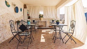 Een terras met zitplaatsen buiten, een stenen muur en een keukenhoek met gordijnen.