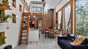 A modern interior with a loft bedroom, a dining area, and a living room with a black sofa and wooden furniture. - Simply Nature in the City (Smyrna)