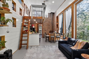 Ein modernes Interieur mit Schlafgalerie, Essbereich und Wohnzimmer mit schwarzem Sofa und Holzmöbeln.