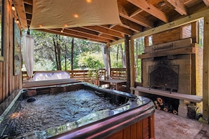 Ein Whirlpool, ein Kamin und eine Holzterrasse mit Blick auf Bäume.