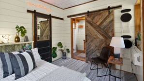 A room with a bed, a desk with a lamp, a plant, and a sliding barn door. - Simply Nature in the City (Smyrna)