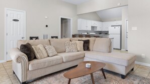 Una sala de estar con un sofá seccional color beige, una mesa de centro de madera y un tapete estampado.