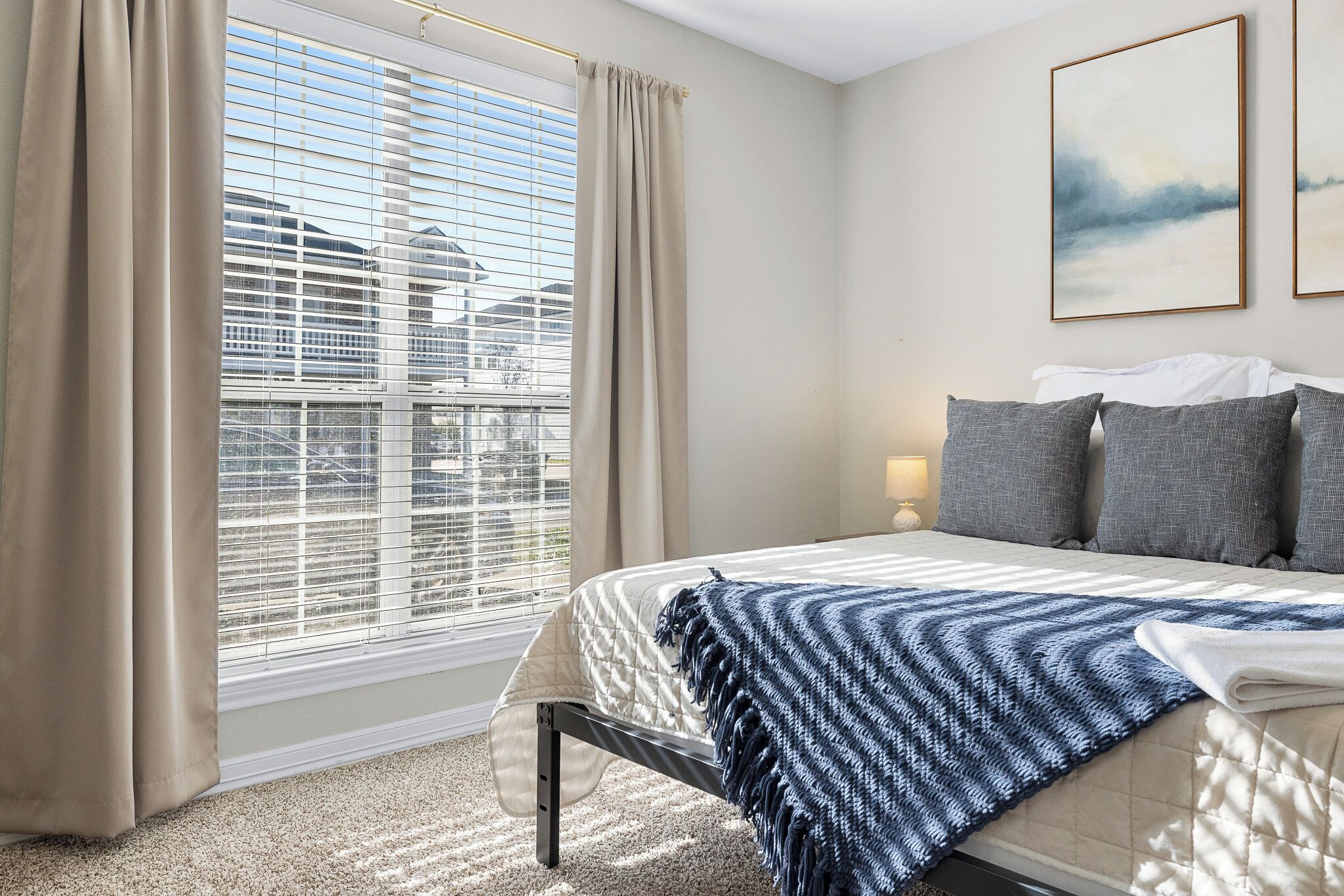 A bedroom with a bed, curtains, a window with blinds, and a painting on the wall.
