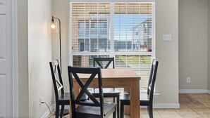 Un comedor con mesa de madera y cuatro sillas, una ventana con persianas y una lámpara de pie.