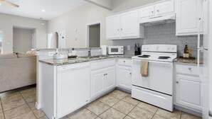 Una cocina moderna con armarios blancos, microondas integrado, estufa y lavavajillas.
