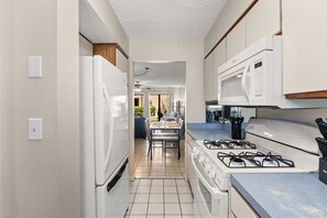 Eine schmale Küche mit Kühlschrank, Herd, Mikrowelle und Essbereich, der auf eine Terrasse hinausführt.