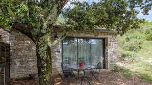 Un edificio de piedra con puerta de vidrio, una mesa redonda con sillas y una planta en maceta.
