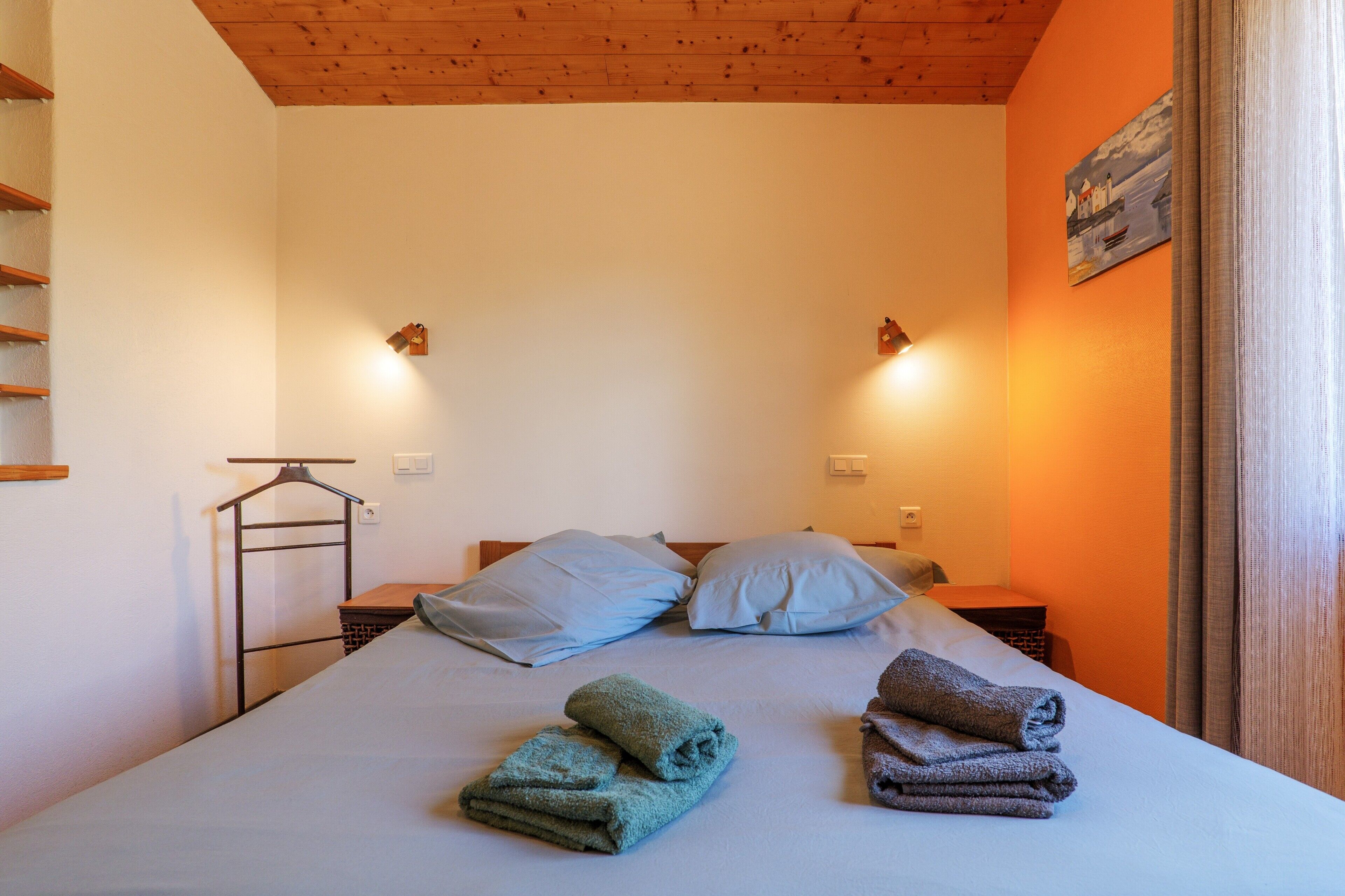Ein Schlafzimmer mit einem Bett, Kissen, einem Nachttisch, einer Wandleuchte und einem Bild.