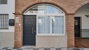 Un edificio con una porta nera, una finestra con tenda e un ingresso piastrellato.