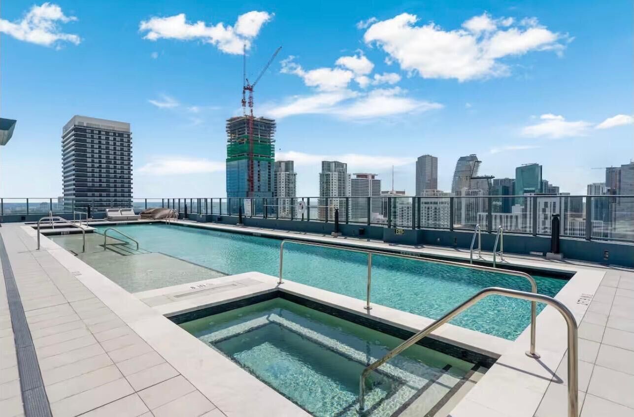 A rooftop swimming pool with a city skyline view, a high-rise building, and a construction crane in the background.