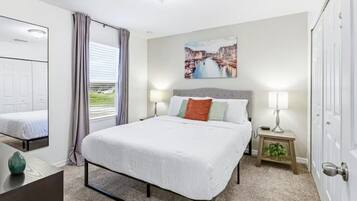 Une chambre d’hôtel avec un lit, des tables de chevet, une fenêtre avec des rideaux, un tableau au mur et une porte.