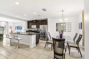 A modern kitchen with a central island, stainless steel appliances, and a dining area with a glass table and chairs. - Orlando Family Retreat Near Disney Magic (Davenport)