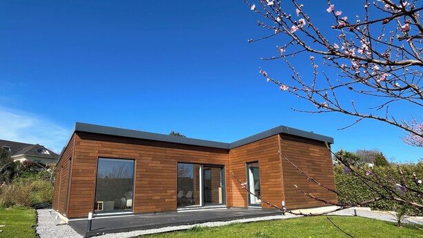 Een modern huis met twee verdiepingen, grote ramen, een plat dak en een verzorgd gazon.