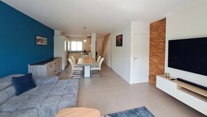 A modern living room with a sofa, TV, and dining area. - Le Refuge Balnéaire - À 3km de la plage (Pornichet)